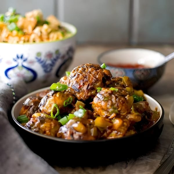 A bowl of Manchurian with green onions, with a blurred bowl of noodles in the background.