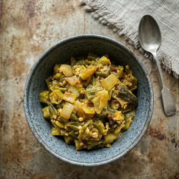 Overhead view of a blue bowl filled with cooked okra and onions, beside a spoon and napkin.